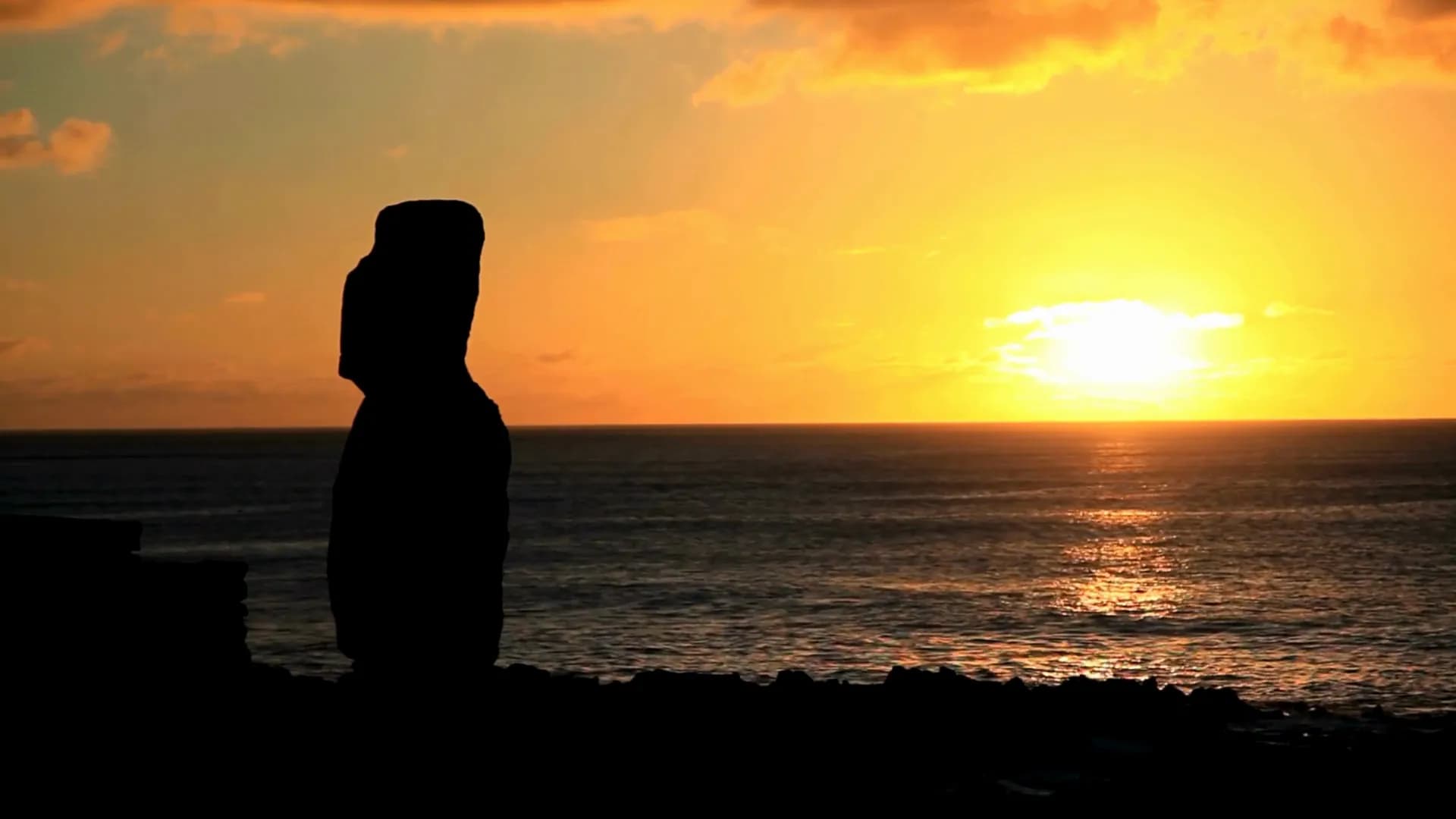 Silueta de un moái contra el atardecer en el mar